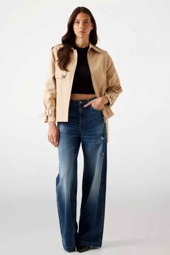 Kurzer Damen-Trenchcoat in Beige über schwarzem Croptop mit Wide-Leg-Jeans, Vollkörperaufnahme im Studio.