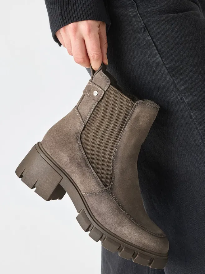 Taupefarbener Chelsea Boot aus Wildleder mit Chunky-Profilsohle, seitlichem Elastik-Einsatz und Anziehschlaufe in Hand gehalten