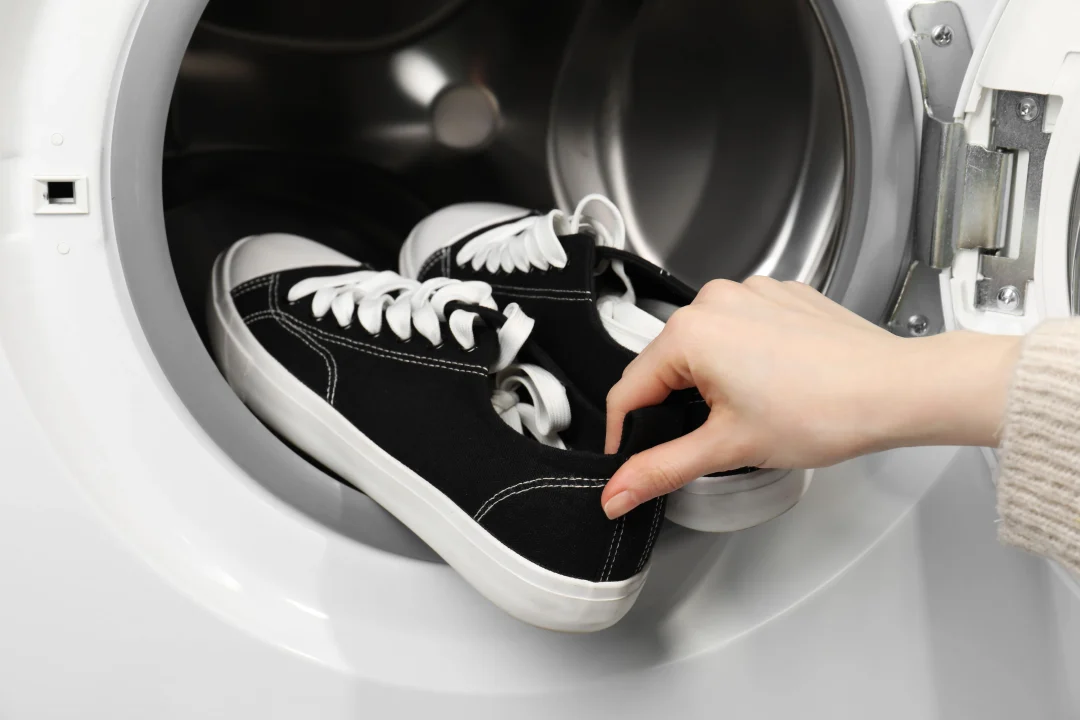 Sneaker waschen: schwarze Canvas-Sneaker werden in eine Waschmaschine gelegt, Nahaufnahme einer Hand an der Ferse