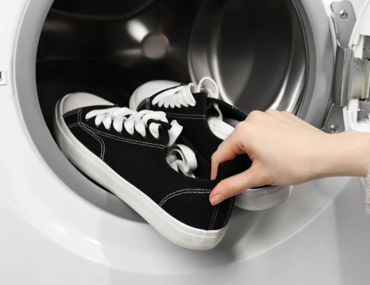 Sneaker waschen: schwarze Canvas-Sneaker werden in eine Waschmaschine gelegt, Nahaufnahme einer Hand an der Ferse