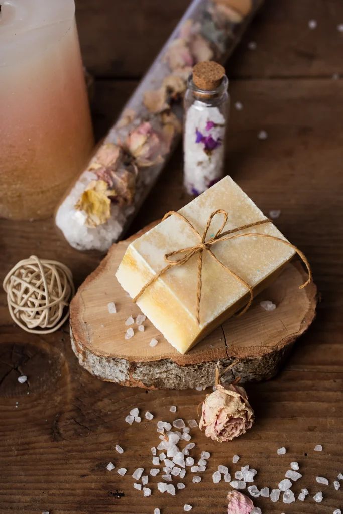 Rustikales Spa-Setup mit fester Seife auf Holzscheibe, Meersalz, Trockenblüten und Kerze – stimmiges Motiv für tallow-Seife/Naturkosmetik