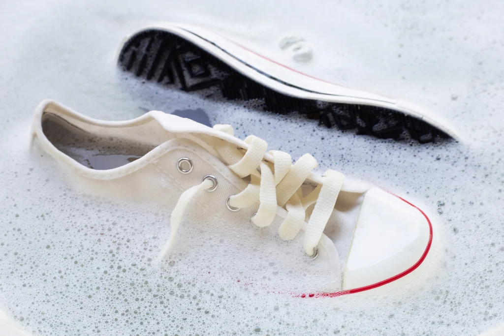 Sneaker waschen: weißer Canvas-Sneaker wird in Seifenlauge per Hand gereinigt, Nahaufnahme mit Schnürsenkeln