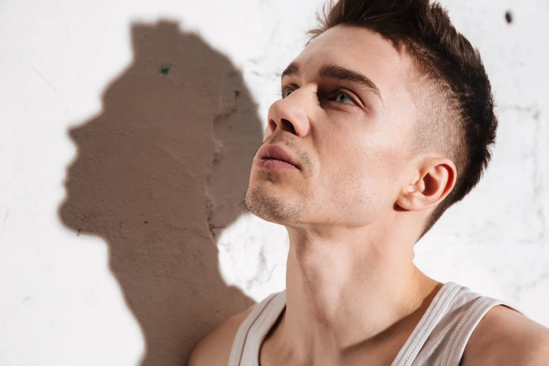 Symbolbild Low Fade: junger Mann mit sauber verblendetem Fade-Haarschnitt, Seiten kurz, Blick nach oben an einer Betonwand