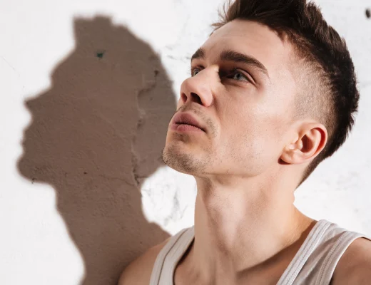 Symbolbild Low Fade: junger Mann mit sauber verblendetem Fade-Haarschnitt, Seiten kurz, Blick nach oben an einer Betonwand