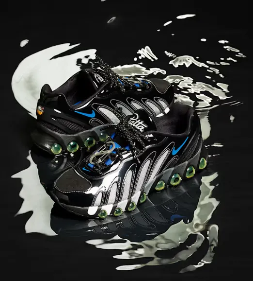 Paar des Patta x Nike Air Max DN8 auf schwarzer, spiegelnder Oberfläche mit Metallic-Panels und grünen Air-Kapseln.