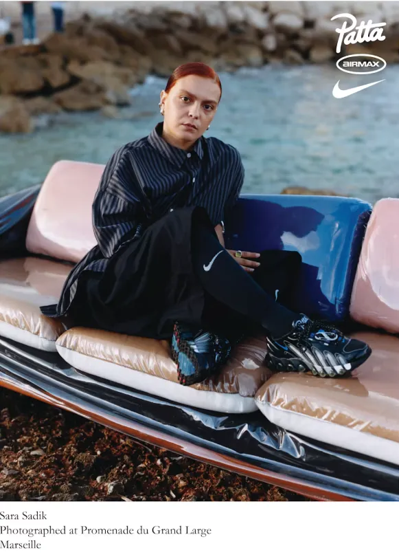 Sara Sadik trägt den Patta x Nike Air Max DN8 an der Promenade du Grand Large in Marseille, sitzend auf einem Sofa am Felsenstrand.