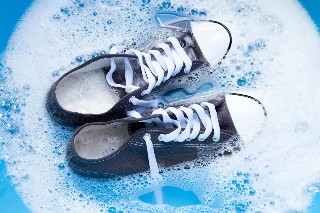 Sneaker waschen: zwei dunkle Canvas-Sneaker werden in Seifenlauge eingeweicht, Vorbereitung zur Handwäsche