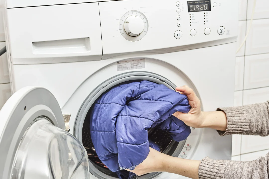 Daunenjacke waschen: blaue Steppjacke wird in eine Frontlader-Waschmaschine gelegt