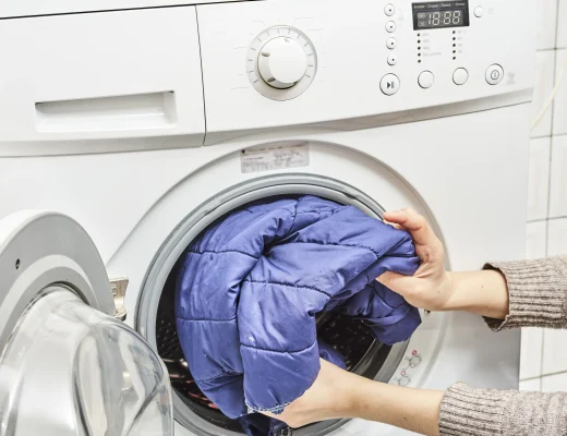 Daunenjacke waschen: blaue Steppjacke wird in eine Frontlader-Waschmaschine gelegt