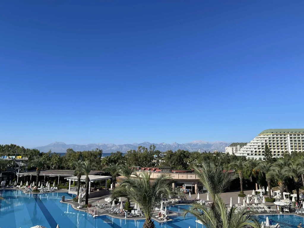 Weitläufige Hotelanlage mit Palmen, Pools und Bergkulisse an der türkischen Riviera – perfektes Ziel für spontane Last-Minute-Reisen in die Sonne.