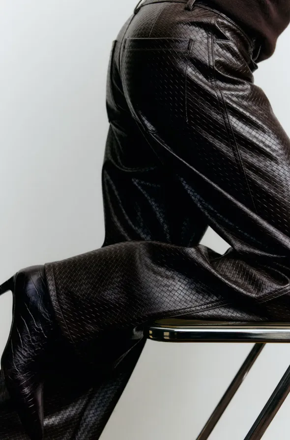Dunkelbraune Lederhose mit strukturierter Oberfläche in Nahaufnahme, kombiniert mit dunklem Oberteil und Absatzschuh.