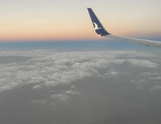 Flugzeugflügel über einer hellen Wolkendecke im Abendlicht auf einem spontanen Last-Minute-Flug Richtung Süden.