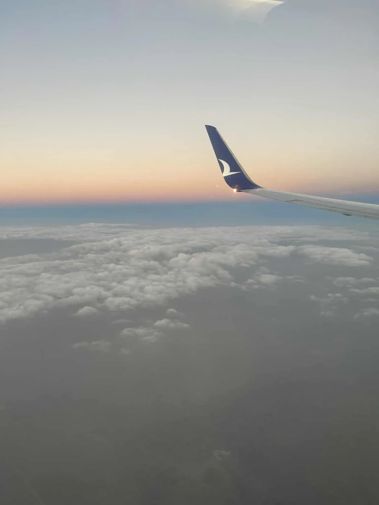 Flugzeugflügel über einer hellen Wolkendecke im Abendlicht auf einem spontanen Last-Minute-Flug Richtung Süden.