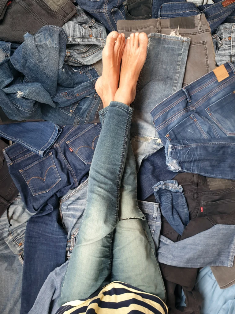 Person sitzt auf einem großen Haufen verschiedener Jeansmodelle und trägt eine hellblaue Skinny Jeans.