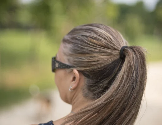 Frau mit zusammengebundenem langen Haar in einem glatten Pferdeschwanz, von hinten fotografiert, beim Spaziergang im Grünen.