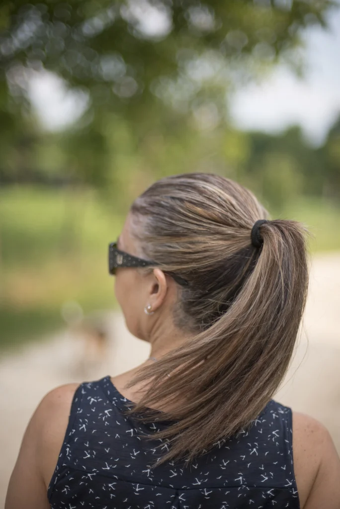 Frau mit zusammengebundenem langen Haar in einem glatten Pferdeschwanz, von hinten fotografiert, beim Spaziergang im Grünen.