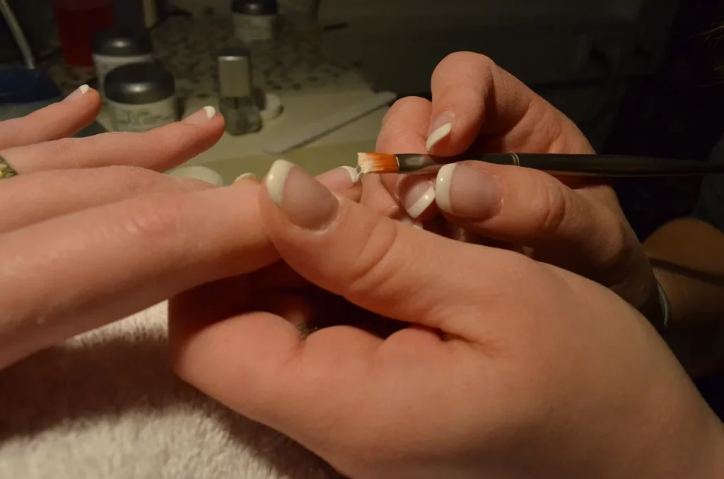 French Nails werden im Nagelstudio präzise mit Pinsel gestaltet, klassische weiße Spitzen auf natürlichem Nagelbett