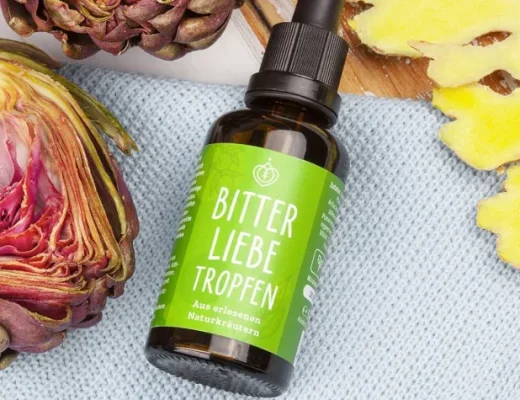BitterLiebe Bittertropfen in Glasflasche mit grünem Etikett, umgeben von Artischocke und Ingwer