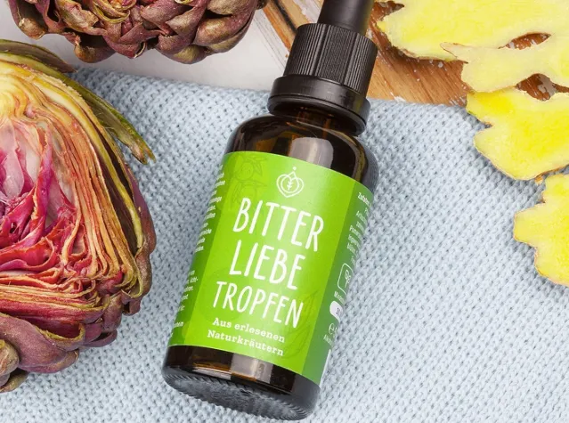 BitterLiebe Bittertropfen in Glasflasche mit grünem Etikett, umgeben von Artischocke und Ingwer