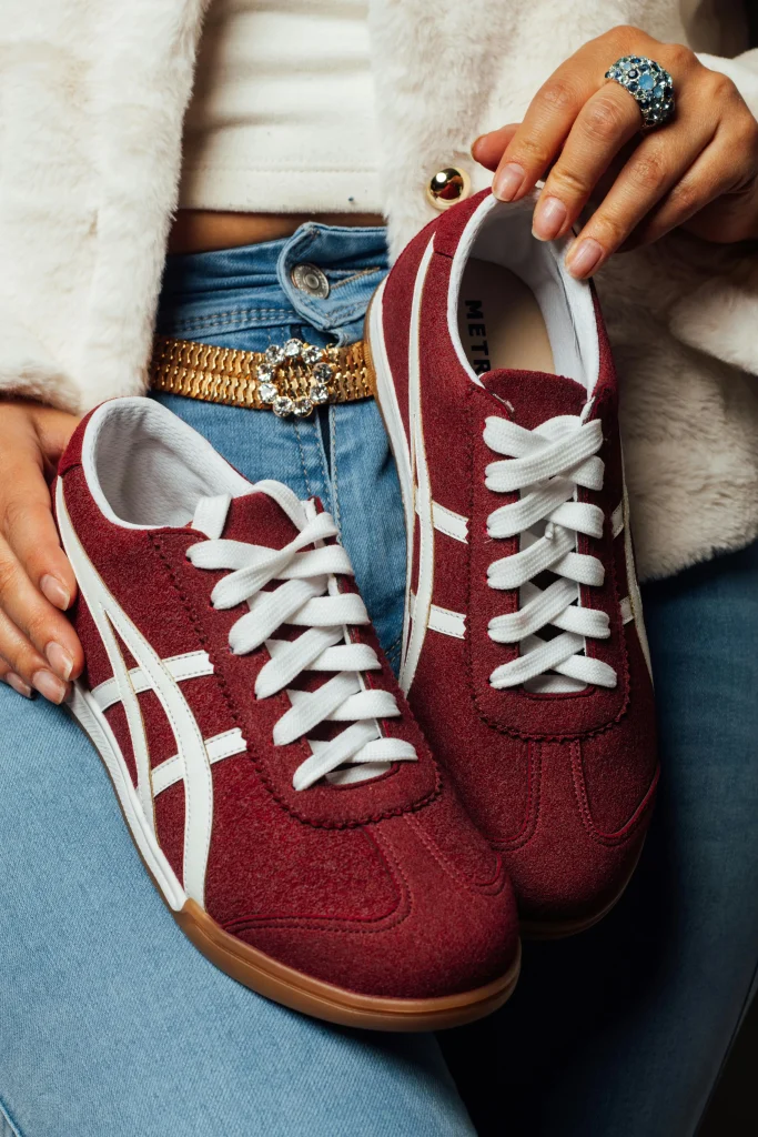 Sportlicher Damen-Sneaker in Bordeauxrot mit weißer Schnürung, kombiniert mit Jeans und modischen Accessoires