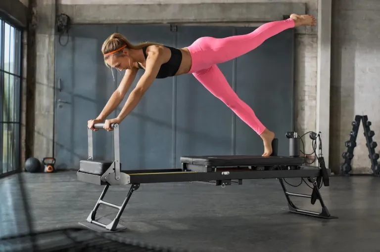 Frau trainiert eine anspruchsvolle Gleichgewichts&uuml;bung beim Reformer-Pilates auf einem Pilates-Reformer