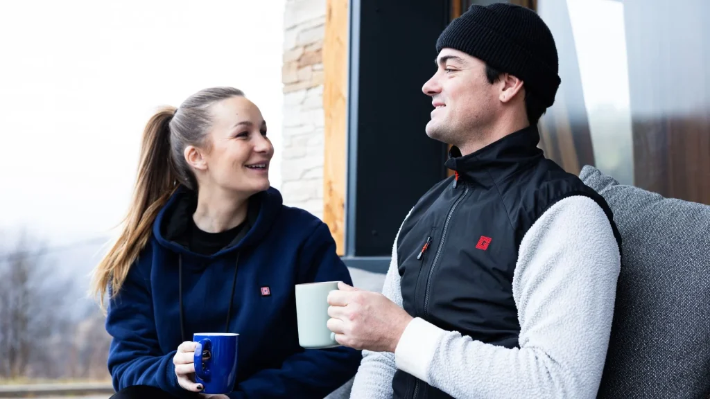 Ein Paar hält Tassen und unterhält sich im Freien, während sie G-Heat-Kleidung tragen.