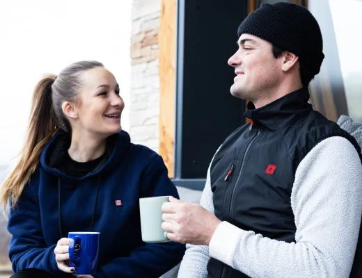 Ein Paar hält Tassen und unterhält sich im Freien, während sie G-Heat-Kleidung tragen.