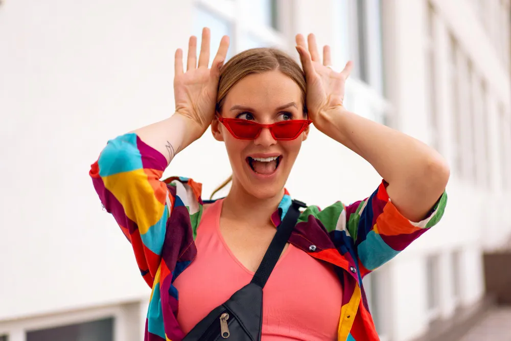 Frau mit buntem Outfit und roter Sonnenbrille zeigt Dopamine Dressing mit verspielter Pose