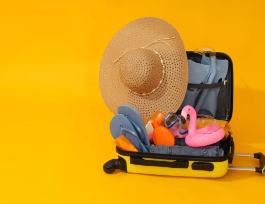 Ein gelber Koffer mit Sommeraccessoires wie Strohhut, Sonnenbrille und Schwimmflügel