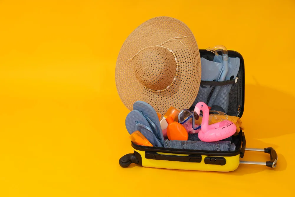 Ein gelber Koffer mit Sommeraccessoires wie Strohhut, Sonnenbrille und Schwimmflügel