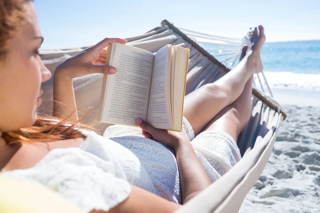 Frau liest ein Buch in einer Hängematte am Strand während des Sommerurlaubs