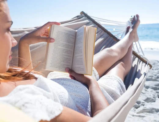 Eine Frau liegt in einer Hängematte am Strand und liest ein Buch