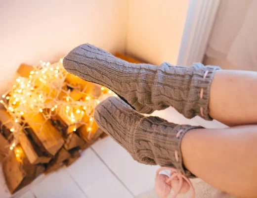 Ein Paar graue Socken vor einem dekorativen Hintergrund mit Holzscheiten und Lichterketten.