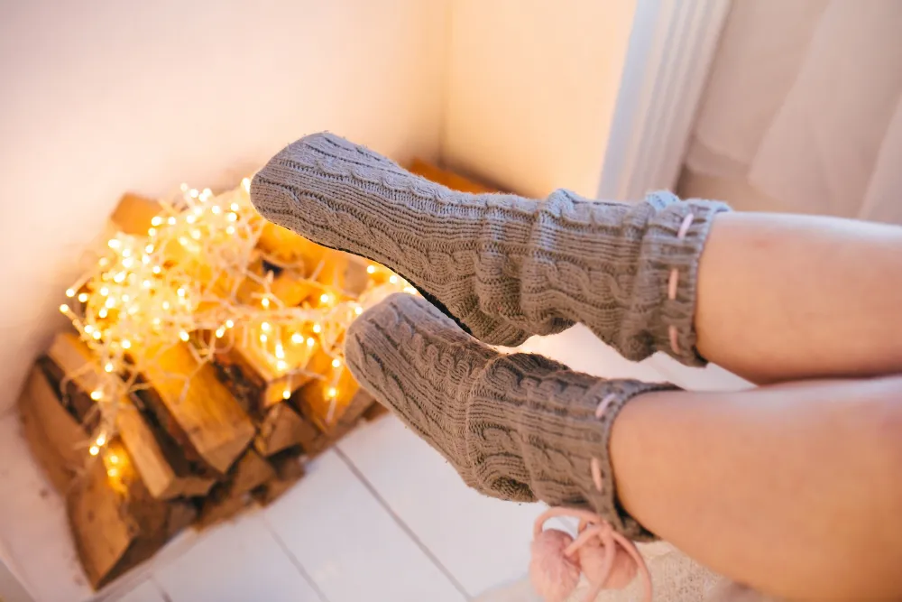 Ein Paar graue Socken neben einem dekorativen Holzstapel mit Lichterkette