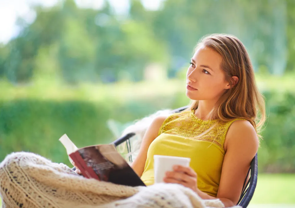 Junge Frau liest ein Buch auf einer Terrasse und genießt einen entspannten Sommertag