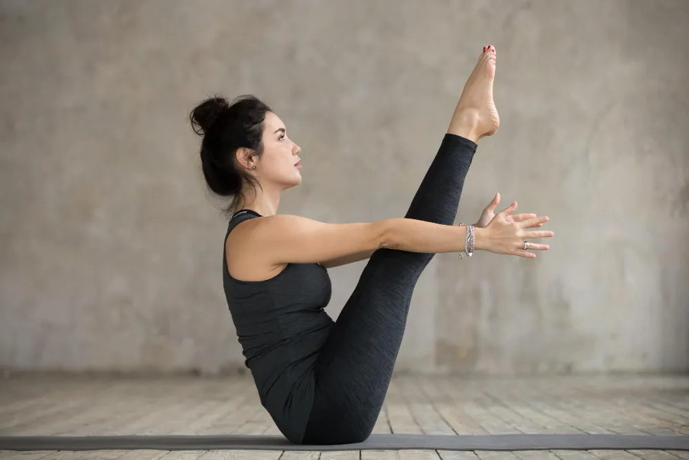 Frau hält die Yoga-Pose Paripurna Navasana mit gestreckten Beinen auf einer Yogamatte