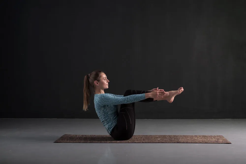 Frau hält die Yoga-Pose Ardha Navasana auf einer Yogamatte und trainiert ihre Körpermitte