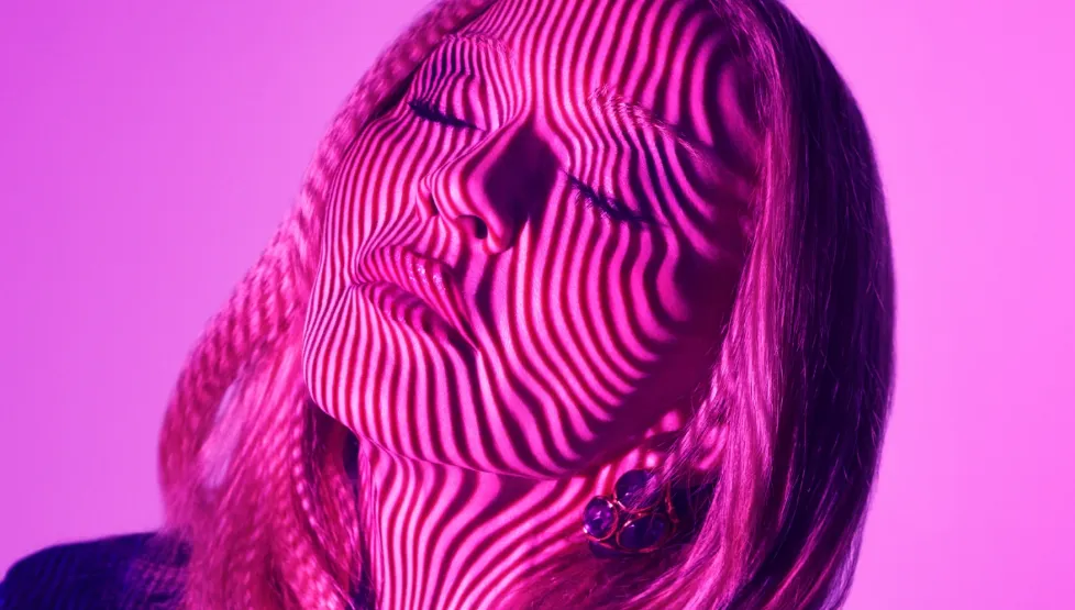 Nahaufnahme eines weiblichen Gesichts im pinkfarbenen Licht, über das wellenförmige Schattenlinien verlaufen – Kampagnenmotiv von KIKO Milano.