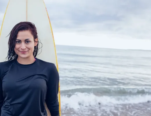 Dame im schwarzen Rashguard mit Surfbrett am Strand