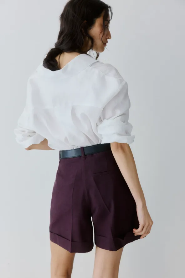 Bordeauxfarbene Tailored Shorts mit weißer Bluse und schwarzem Gürtel als eleganter Sommer-Look fürs Büro