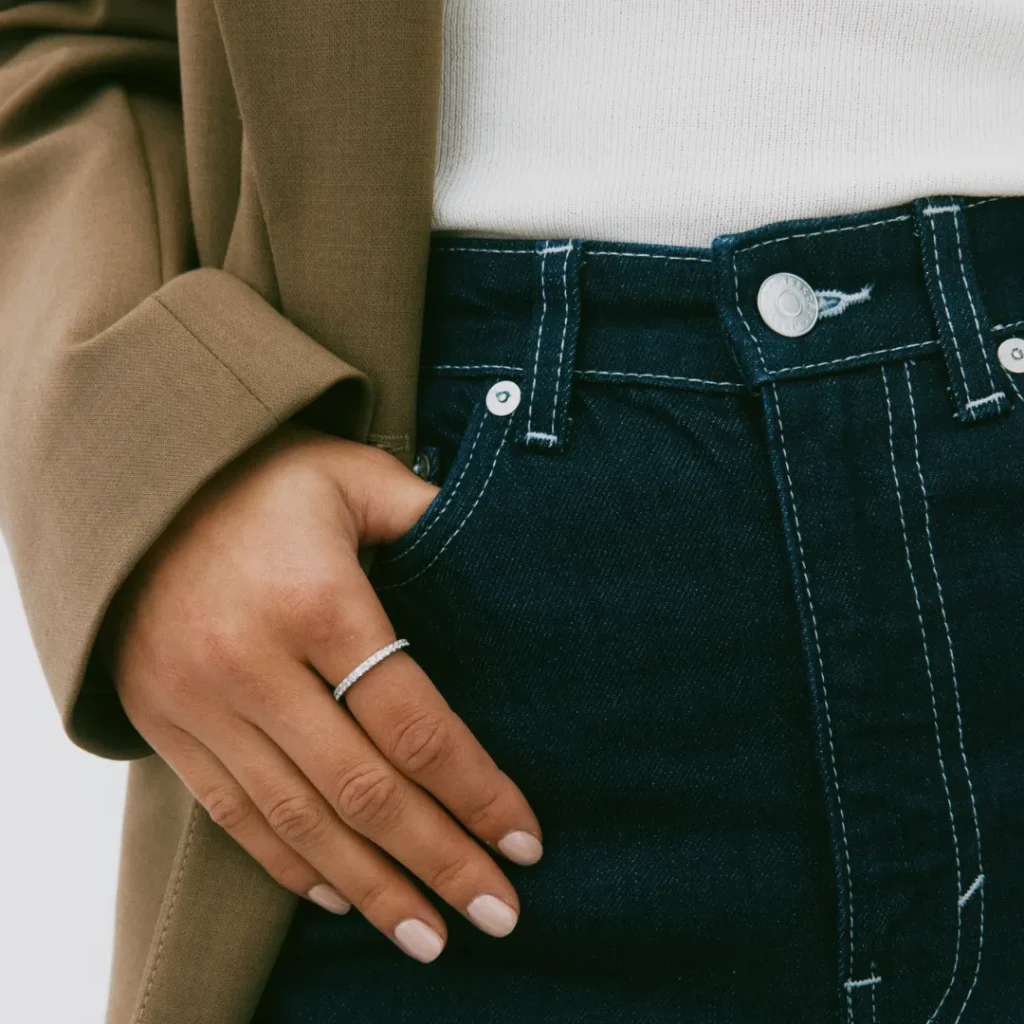 Ein modisches Beispiel für Layering ohne Überladen: Eine Hand mit minimalistischem Schmuck in einer Tasche