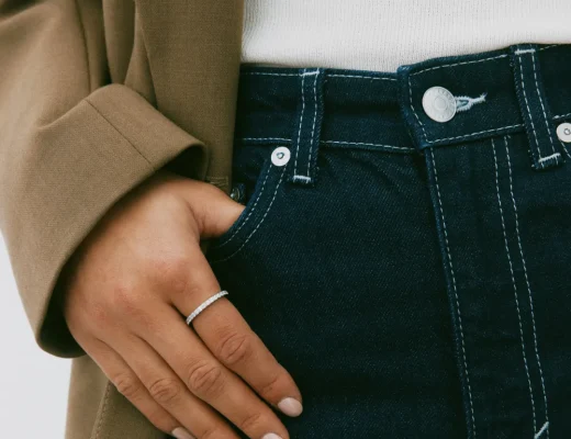 Ein modisches Beispiel für Layering ohne Überladen: Eine Hand mit minimalistischem Schmuck in einer Tasche