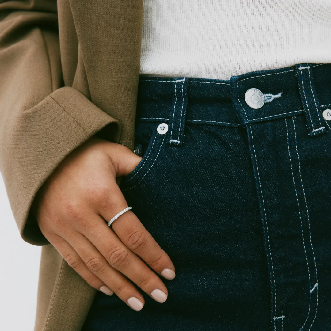 Ein modisches Beispiel für Layering ohne Überladen: Eine Hand mit minimalistischem Schmuck in einer Tasche
