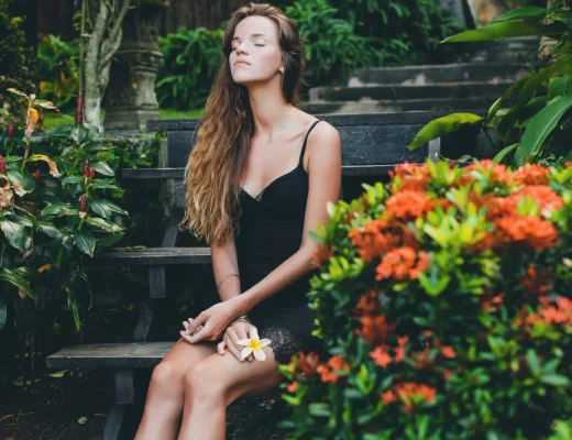 Frau in schwarzem Sommerkleid sitzt zwischen tropischen Pflanzen
