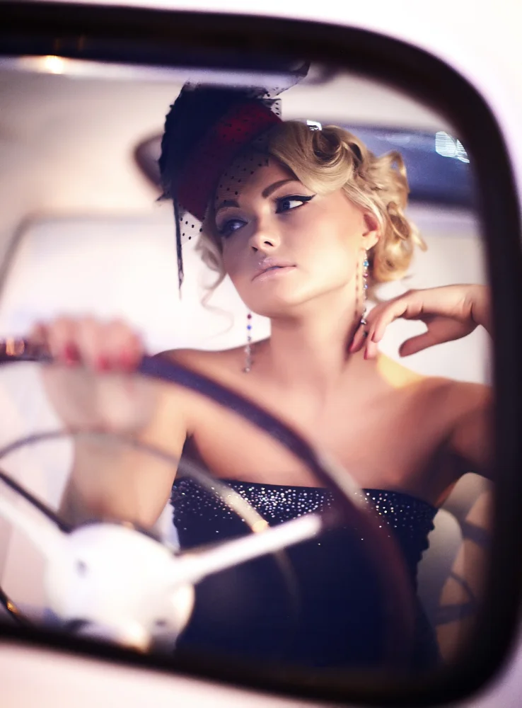 Blonde Frau mit glamouröser Retro-Frisur und Fascinator in einem Auto