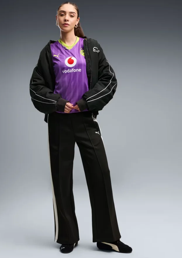 Model trägt das lila Borussia-Dortmund-Ausweichtrikot 2026 mit weiter schwarzer Hose und Jacke als Streetwear-Look.