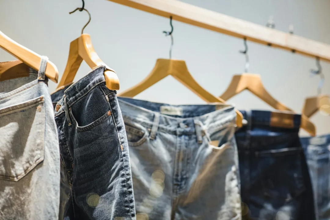 Verschiedene Jeans in verschiedenen Blautönen hängen auf Holzkleiderbügeln an einer Stange