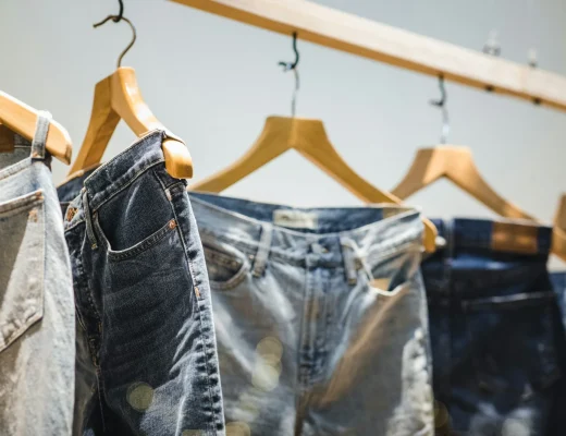 Verschiedene Jeans in verschiedenen Blautönen hängen auf Holzkleiderbügeln an einer Stange