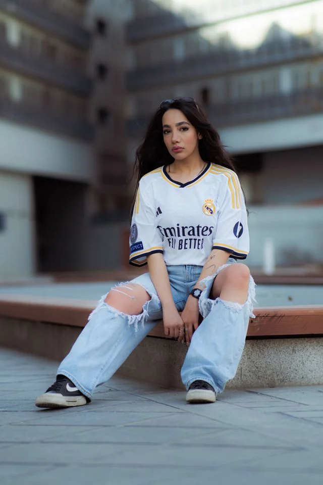 Frau kombiniert ein Fußball-Trikot mit weiter Jeans und Sneakern als Beispiel für den Fußball-Trikot-Mode-Hype.