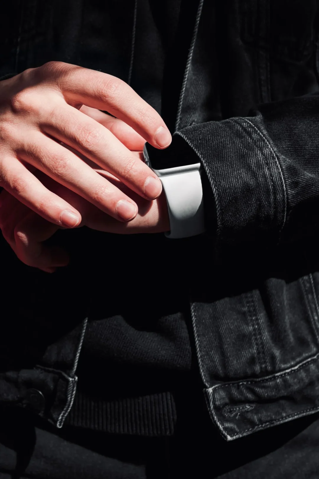Hand in schwarzem Denimärmel mit Smartwatch, Detailaufnahme der Ärmelöffnung und Knopfleiste